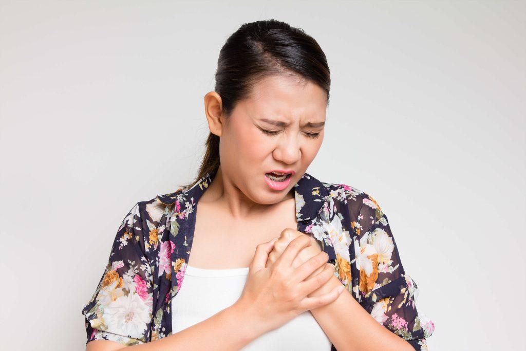 Woman wearing floral shirt holds top of breast and has look of pain on face.